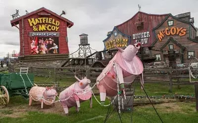 Pink pig decorations on lawn outside Hatfield & McCoy Dinner Feud with wagon and rustic theater building in background