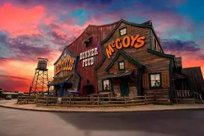 Front view of the Hatfield & McCoy Dinner Feud theater at sunset, with pink and purple clouds illuminating the rustic facade.